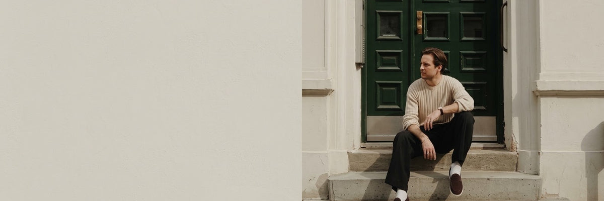 Man in a ribbed knit sweater on stone steps by a green door