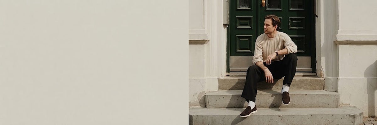 Man in a ribbed knit sweater on stone steps by a green door