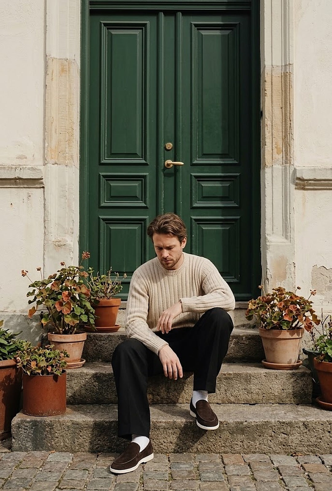 Man in a ribbed knit sweater on stone steps by a green door